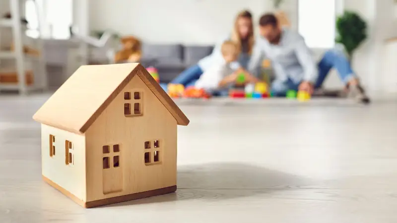 Wooden model house with a family in the background